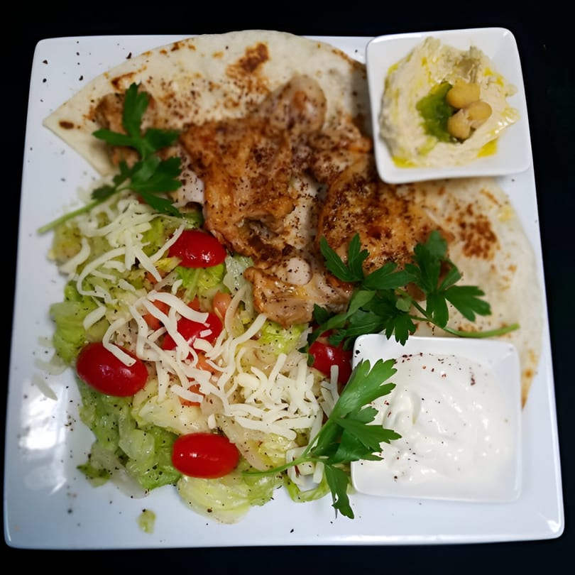 Middle Eastern chicken shawarma with pita, salad, hummus, and garlic sauce on a white plate.