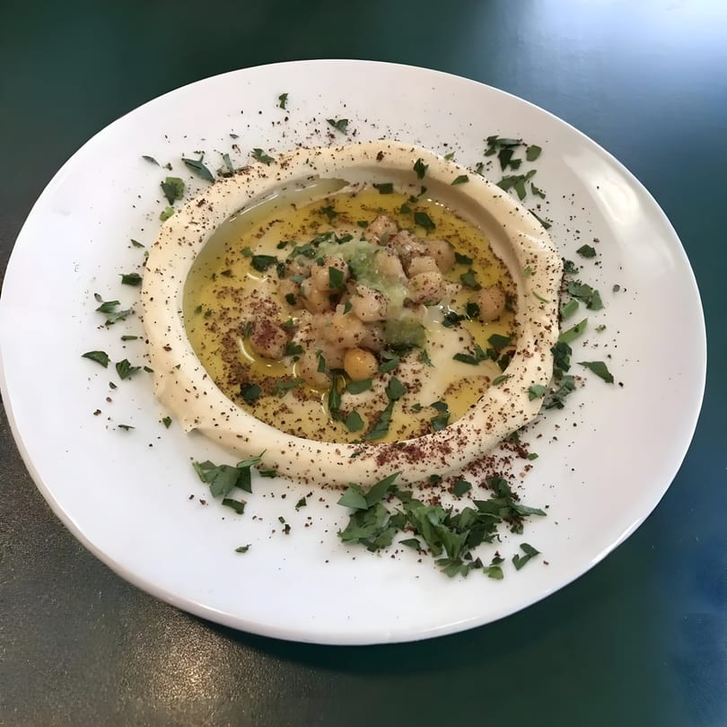 A white plate of Bethlehem Restaurant's hummus, topped with chickpeas, olive oil, and parsley.