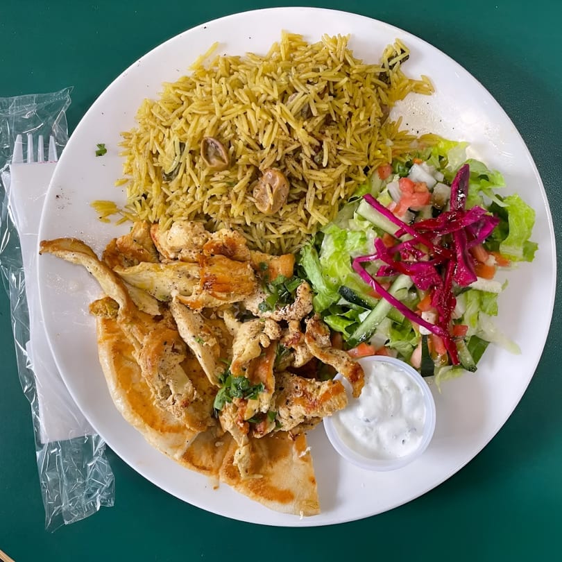 Middle-Eastern chicken shawarma plate with rice, salad, pita bread, and white sauce.